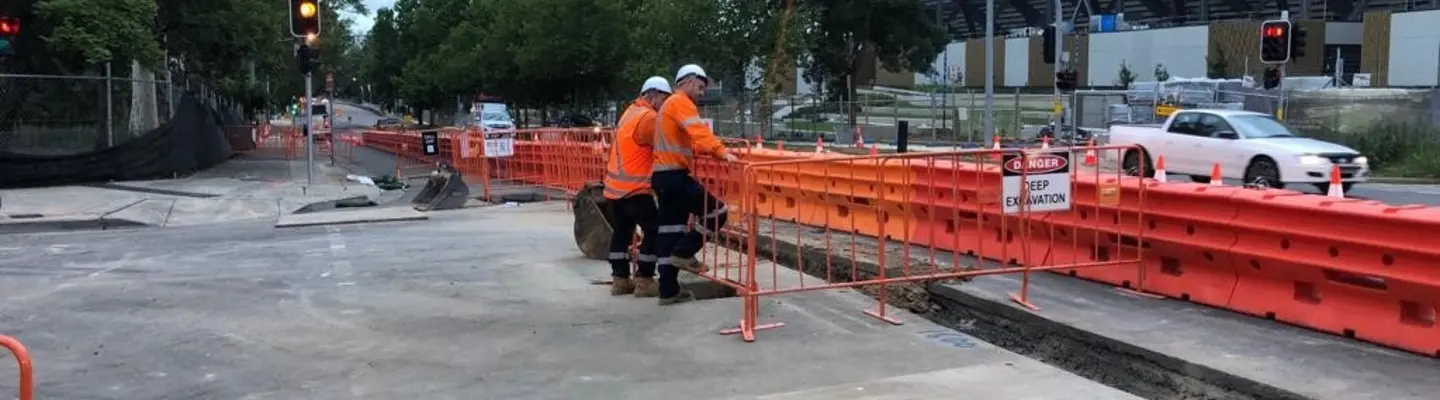 Workers standing in front of installed water-filled safety barriers along a roadside construction zone.