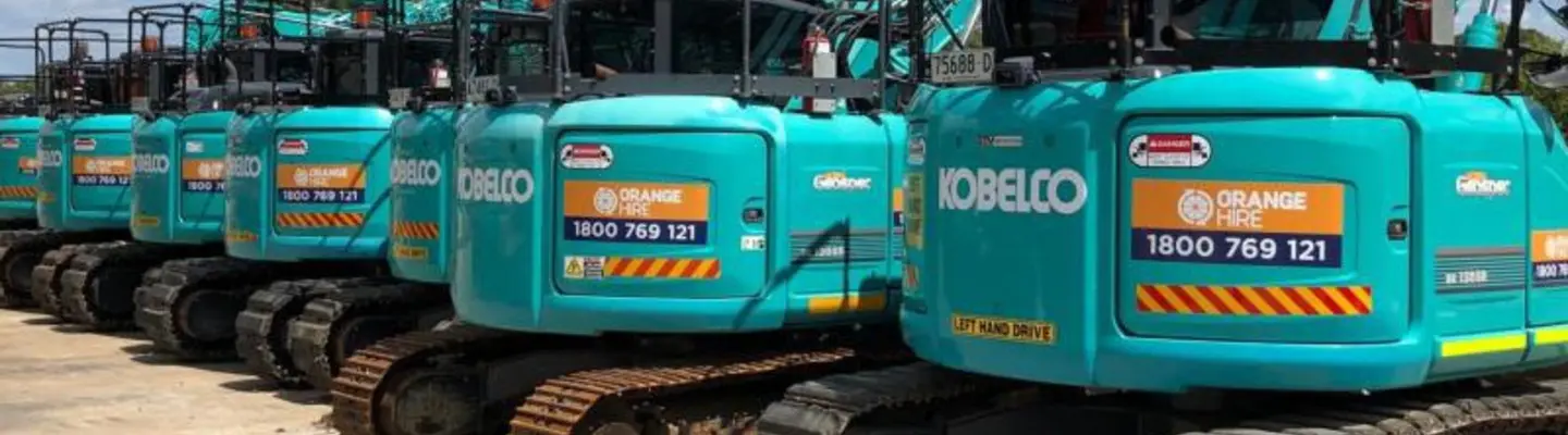 A row of construction equipment lined up on a worksite, inspected and ready for use, with safety barriers in the background.