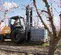 Side view of an orange CASE forklift lifting a water tank. An operator is driving it outdoors on gravel surrounded by trees.