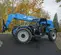 Side view of a blue Genie telehander with retracted boom, forklift attachment and an open cabin outdoors on a paved surface.