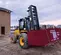 Front angled view of yellow JCB forklift carrying a red cargo container, outdoors at a construction site.