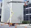 Side view of an orange and beige boom lift with stabilizers next to a building with an operator working on a street light.
