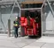 Front view of a red atrium lift with rubber tracks leaving building by a worker in a safety vest on a construction site.