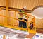 Below angled view of a worker in a yellow safety vest and helmet operating a yellow scissor lift inside a building.