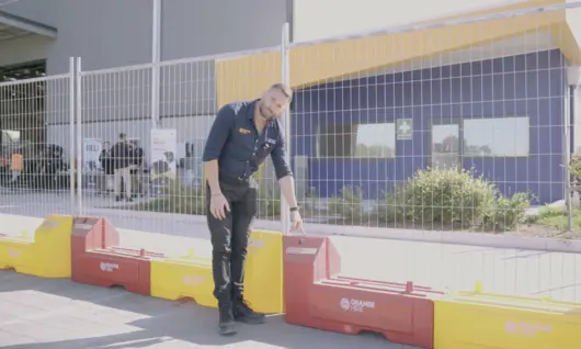 Man in uniform standing inside fencing barriers at a construction site, overseeing safety and site security.