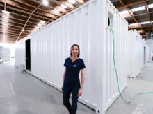 Manager standing in front of stacked containers in a warehouse, overseeing storage and distribution of construction safety barriers.